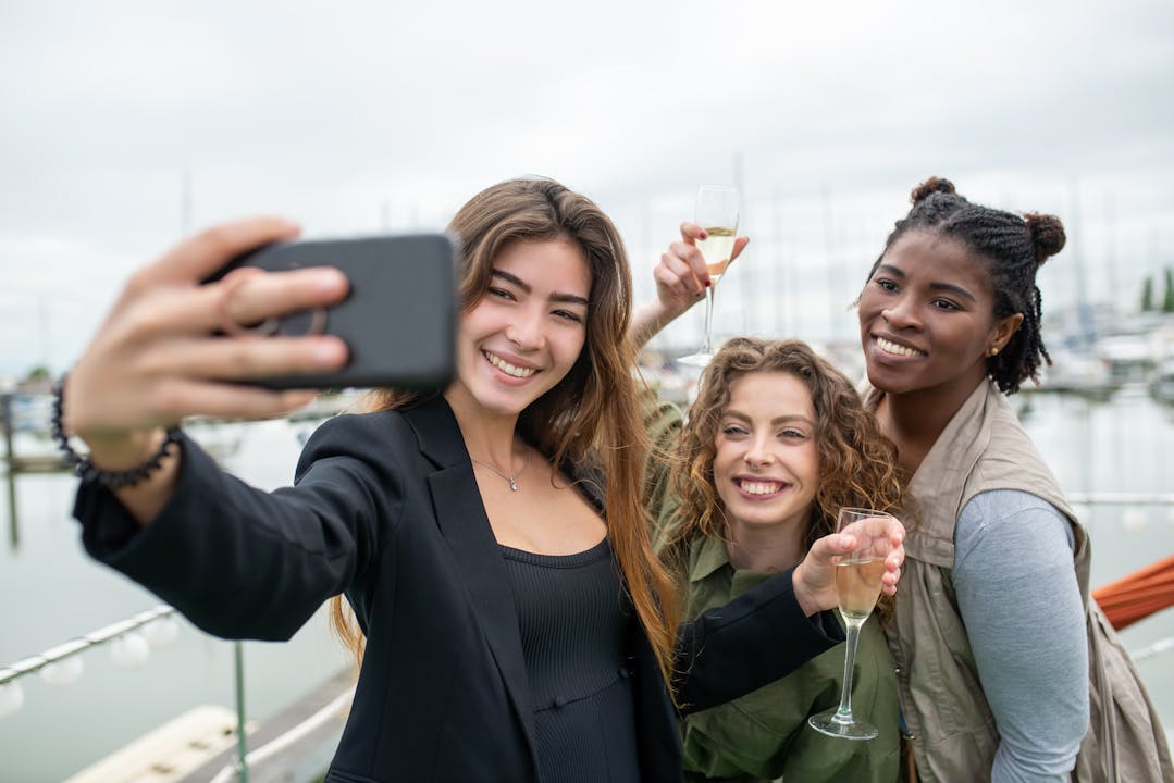 Three women smiling and taking a selfie at a marina